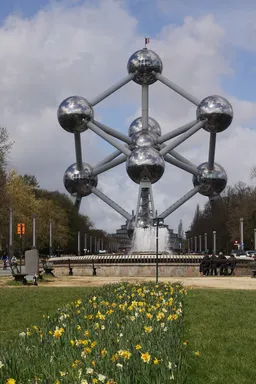 Das Atomium in Brüssel, eine große Skulptur aus spiegelndem Metall welches den Aufbau eines Atoms nachstellt. Kugeln sind in einer hexagonalen Struktur miteinander verbunden, kugelförmig um eine Kugel in der Mitte, dem Atomkern.