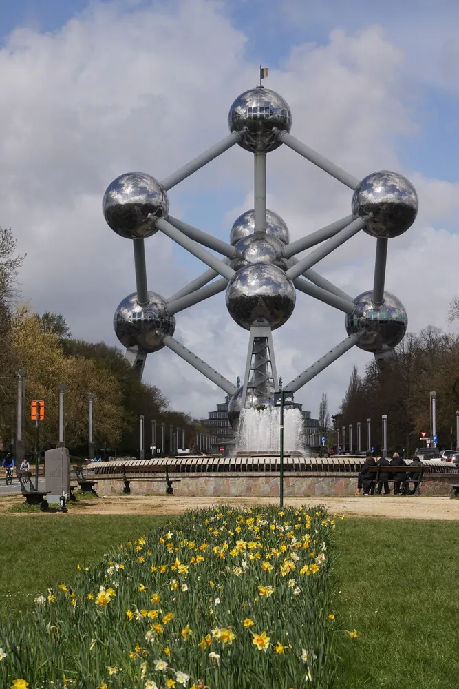 Das Atomium in Brüssel, eine große Skulptur aus spiegelndem Metall, welches den Aufbau eines Atoms nachstellt. Kugeln sind in einer hexagonalen Struktur miteinander verbunden, kugelförmig um eine Kugel in der Mitte, dem Atomkern.