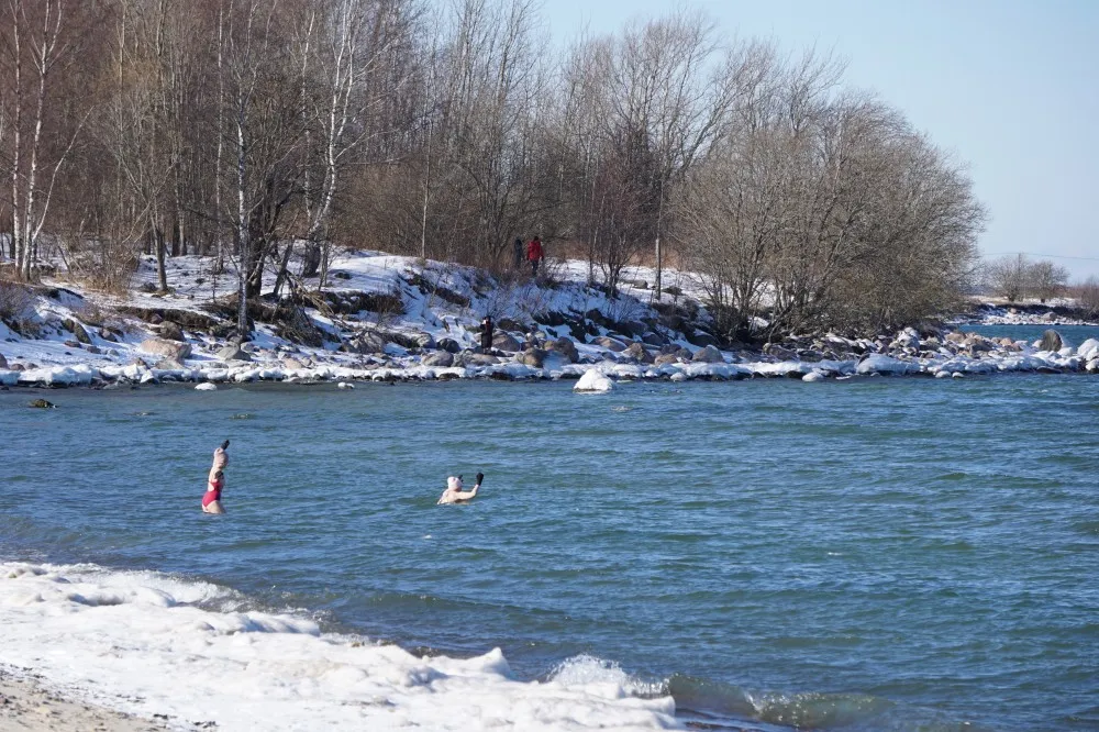 Zwei Frauen gehen im Badeanzug und mit Mütze und Handschuhen gekleidet in das eisige Wasser.