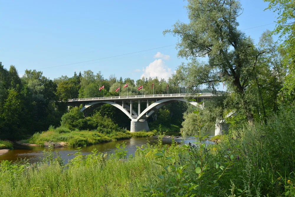 Brücke über einen Fluss mit den Fahnen Lettlands bestehend aus drei großen Bögen.