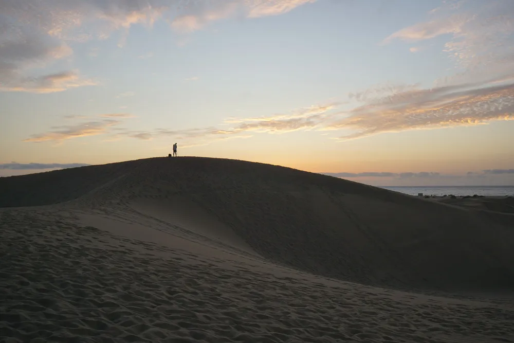 Ein Fotograf steht mit seiner Kamera auf einer Düne und fotografiert den orangen leuchtenden Himmel