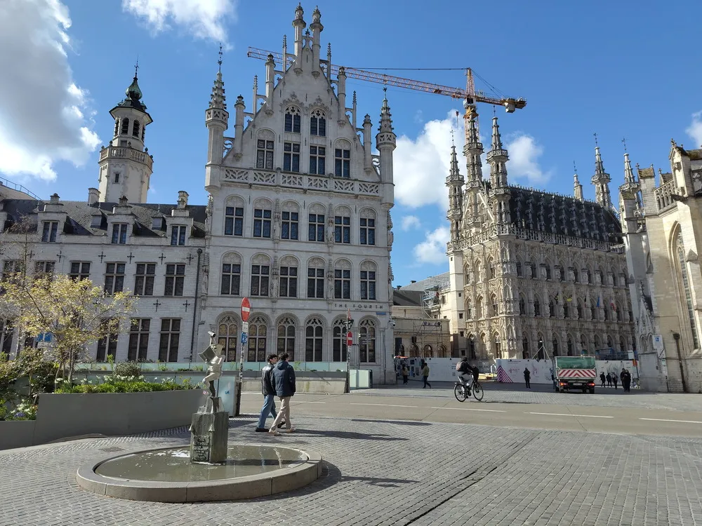 Links ein weißes Gebäude mit 5 Stockwerken und zahlreichen Zier-Türmchen, sowie einem begehbarem Turm. Rechts ein 4-stöckiges Gebäude mit einer Fassade aus zahlreiche Statuen und 6 Türmchen auf dem Dach.