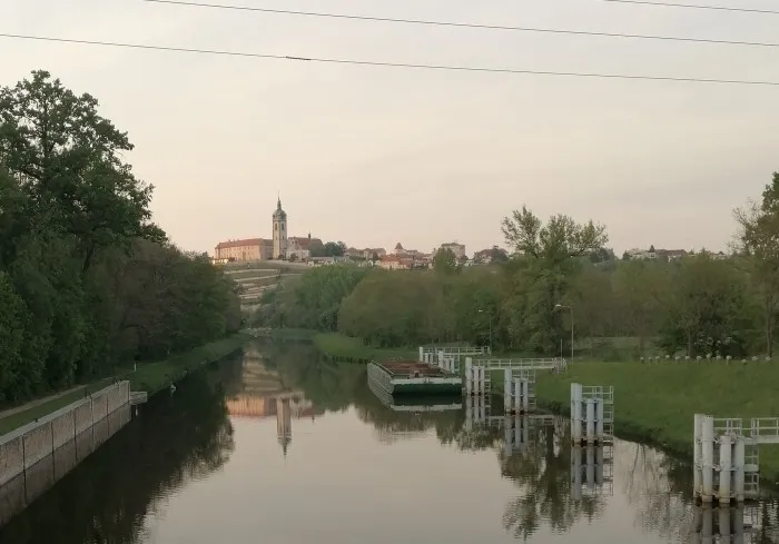 Die letzte Abendsonne strahlt auf das Schloss in Melnik, welches auf einem Berg sitzt. Im Vordergrund ist ein kleiner Kanal.