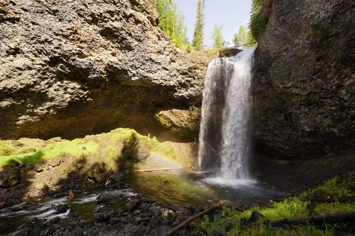 Warmes Sonnenlicht dringt in eine schattige Felsenaushöhlung und bricht sich in dem Wasser eines 35 Meter hohen Wasserfalls.