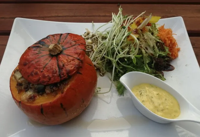 gefüllter Kürbis mit Dip und Salat auf einem weißen Teller