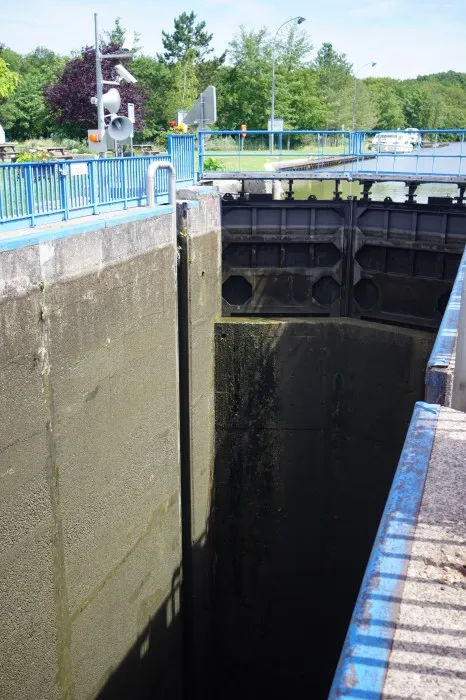 Geschlossenen Schleusentor. Vor dem Tor geht es in einem Betonschacht sehr weit nach unten ins dunkle. Der Boden ist nicht sichtbar. Der Schacht is abgesperrt durch blaue Gitter.