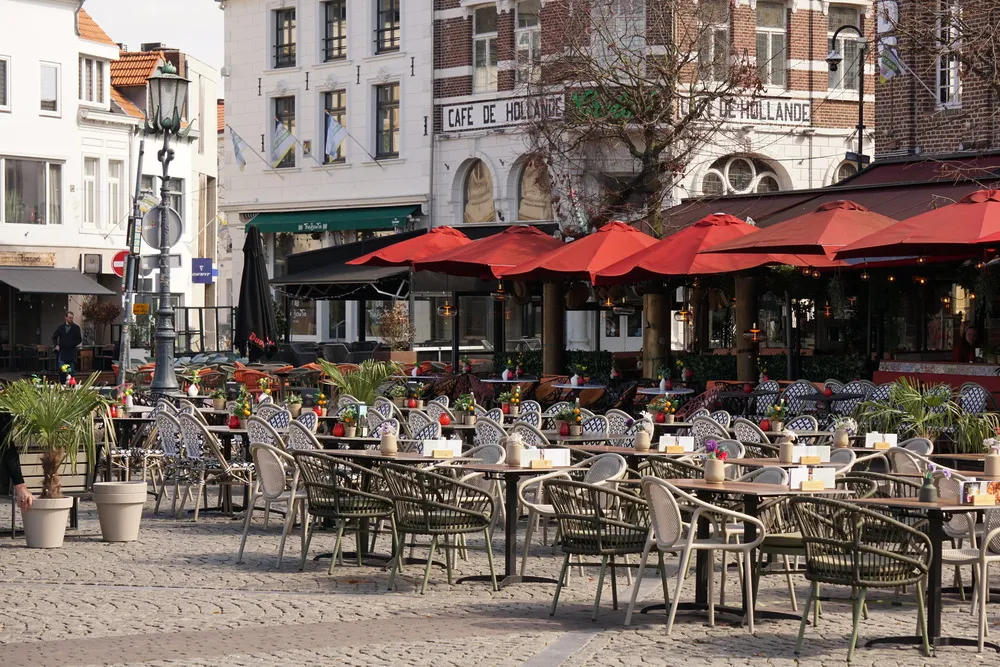 Zahlreiche Stühle vor Restaurants auf einem gepflastertem Marktplatz. Im Hintergrund steht an einem der Häuser "Cafe de Hollande"
