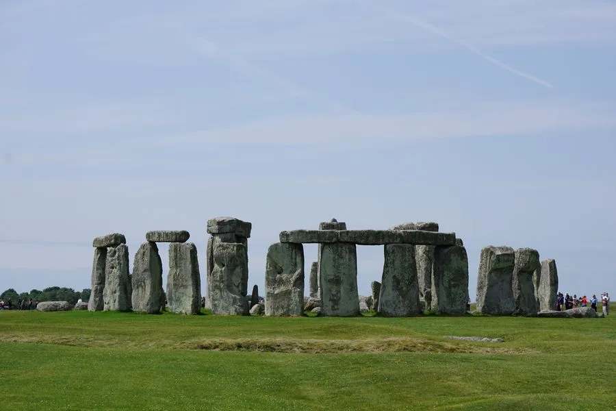 Rechteckige Felsen stehen im Kreis auf einer Wiese. Zwischen manchen liegen weitere große Steine oben drauf und überbrücken die Lücke zwischen ihnen.