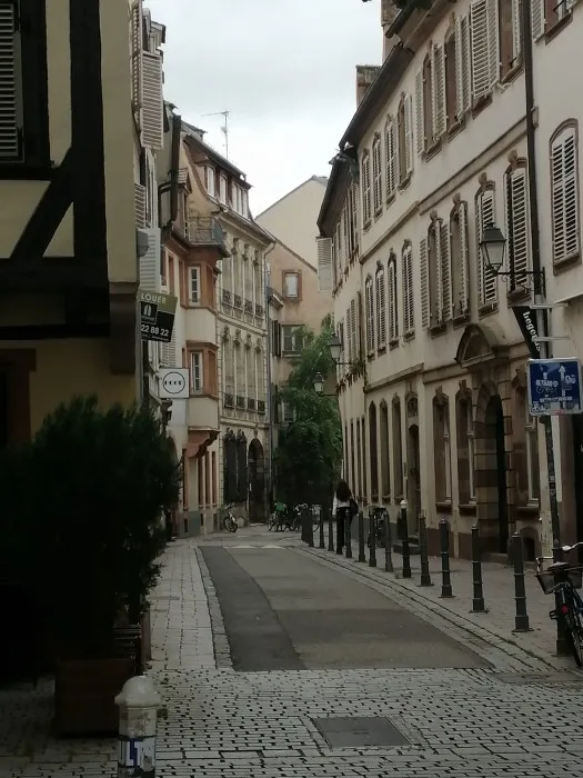 Blick in eine kleine Altstadtgasse. Schiefe Fassaden mit hölzernen Fensterläden in hellen Beige-Tönen.