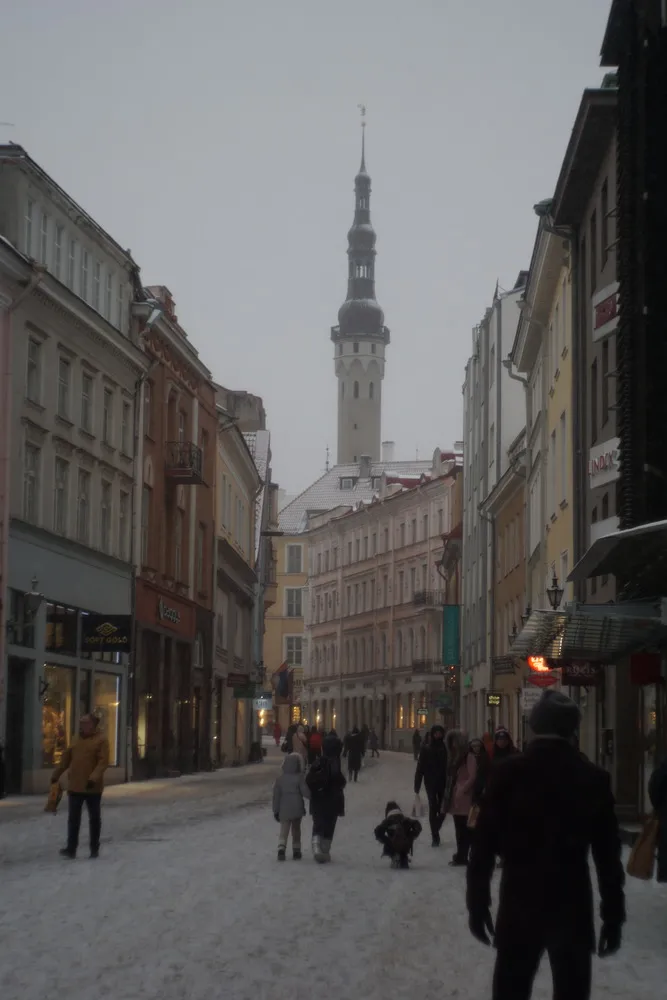 Eine Schneebedeckte Straße durch die Altstadt. Schaufenster leuchten, und im Hintergrund stehte ein schmaler, hoher Kirchturm.