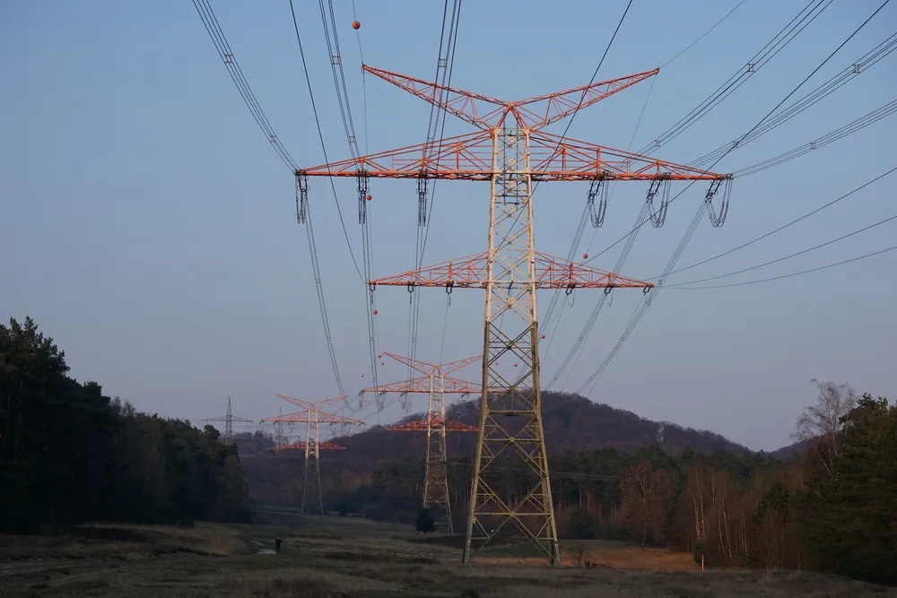Strommasten werden vom Licht der untergehenen Sonne bestrahlt und ziehen durch eine hügelige Waldlandschaft