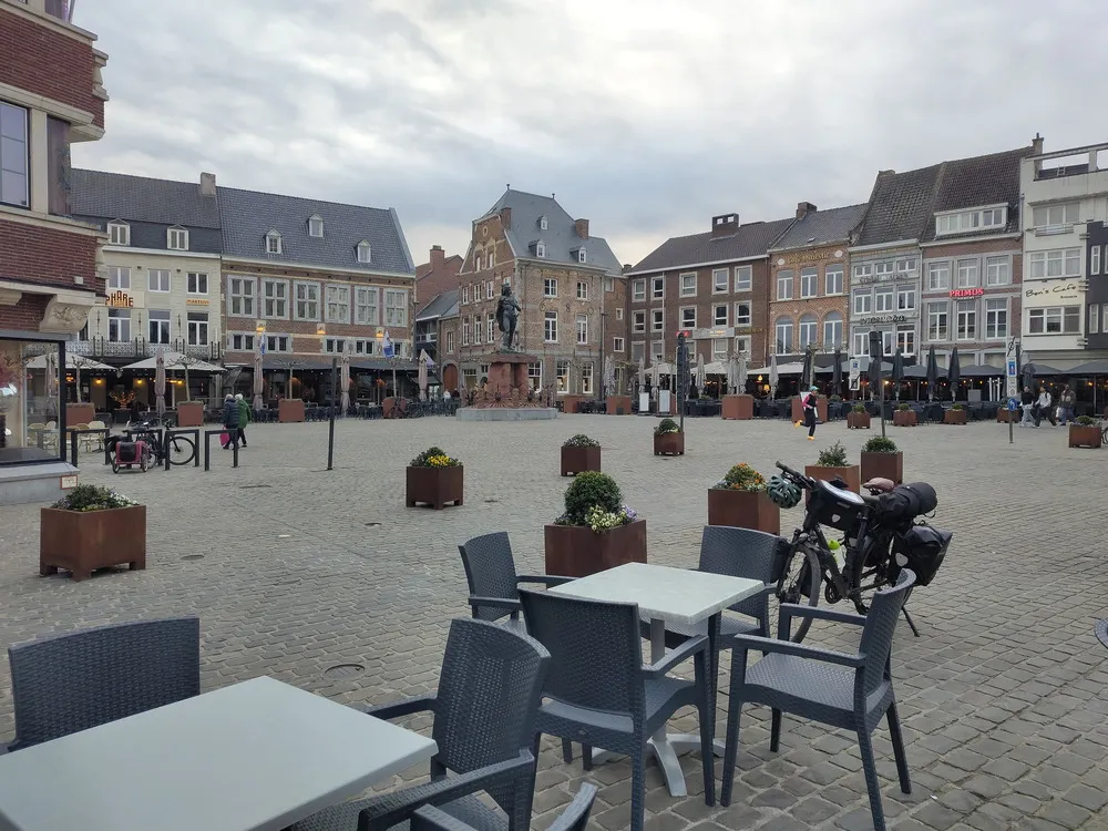 Gepflasterter Marktplatz mit  alten und neuen Häusern. Im Vordergrund Stühle und Tische eines Restaurants sowie das vollgepackte Rad.