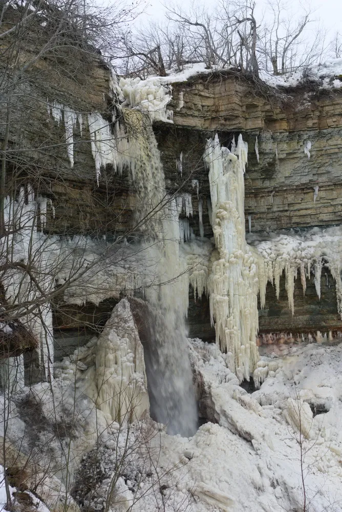 Ein Wasserfall stürzt an einer Felswand aus scheinbar lauter kleinen Würfeln in die tiefe. Ringsherum haben sich Eiszapfen gebildet.