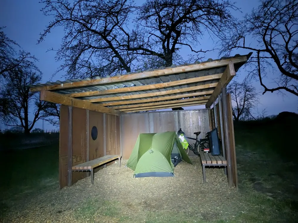 Grünes Zelt und ein Fahrrad bei Dämmerung in einer Schutzhütte